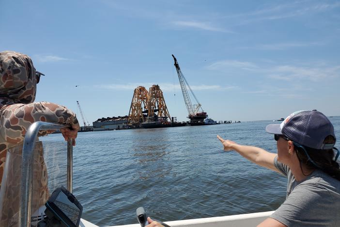 A woman points from a boat, and a man looks, at the wreck of the Golden Ray in St. Simon's Sound