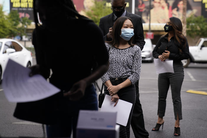 People wait in line, resumes in hand, while waiting to apply for jobs during an outdoor hiring event.