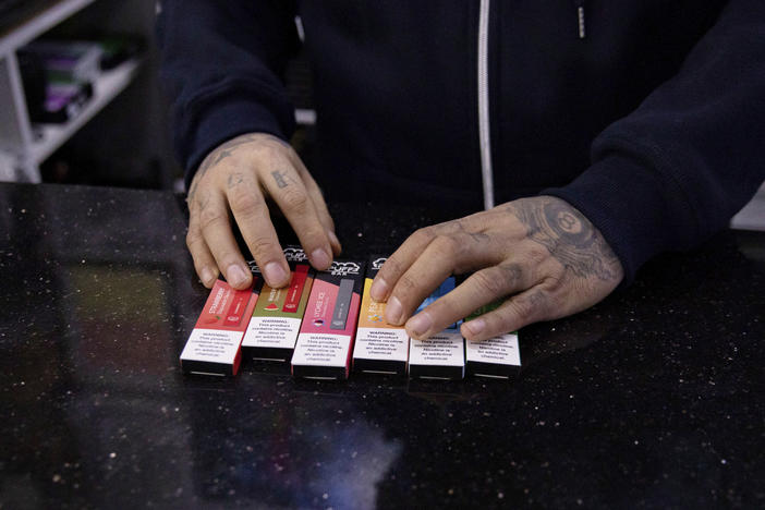 In this Jan. 31, 2020 photo, a vape shop manager shows Puff Bar flavored disposable vape devices at a store in the Brooklyn borough of New York.