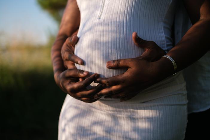 Man's arms embrace a woman's pregnant belly from behind