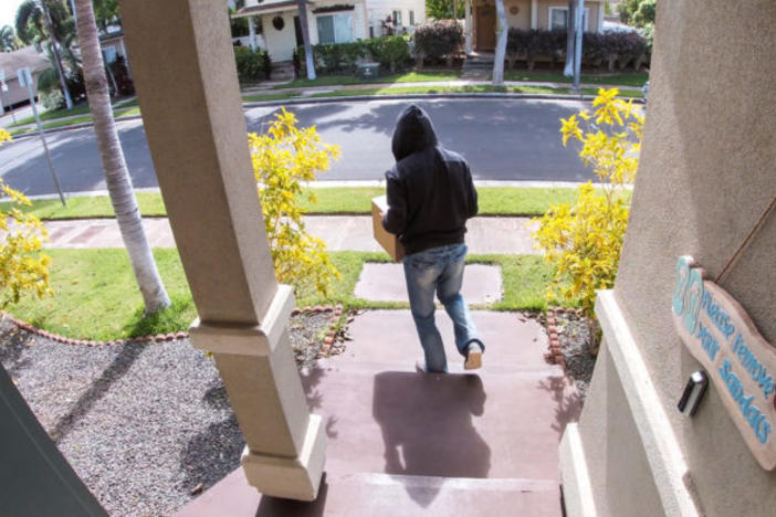 Unidentified person takes a package from a porch