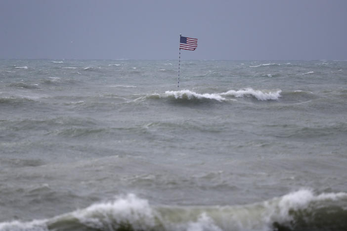 An American flag flies from the shipwreck of the Breconshire, as waves churned up by Tropical Storm Isaias crash around it, Sunday, Aug. 2, 2020, in Vero Beach, Fla. Isaias weakened from a hurricane to a tropical storm late Saturday afternoon, but was still expected to bring heavy rain and flooding as it barrels toward Florida. The Breconshire was a cargo ship that ran aground in 1894.