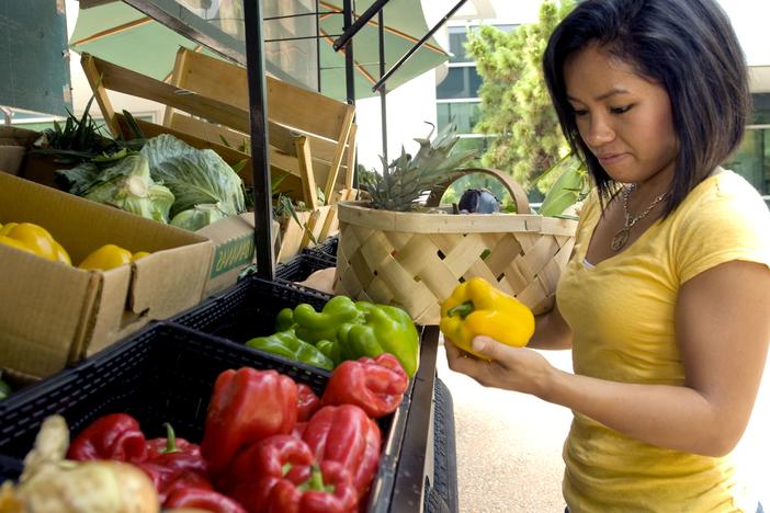 A woman examines a fresh bell pepper at an open-air market.