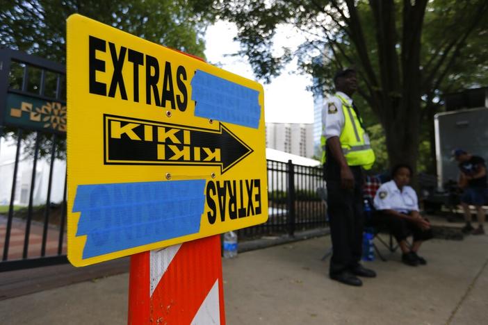 In this Thursday, July 25, 2019 photo, security guards are posted near an entrance to Centennial Olympic Park in downtown Atlanta where a sign for movie extras is set up for Clint Eastwood's film "Richard Jewell."