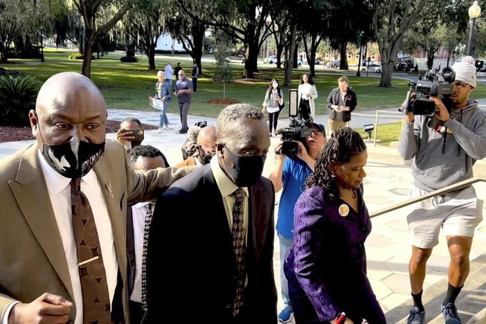 Ahmaud Arbery's father, Marcus Arbery (center), heads into the Glynn County Courthouse in Brunswick, Ga., with his attorney Benjamin Crump on Monday, Oct. 18, 2021.