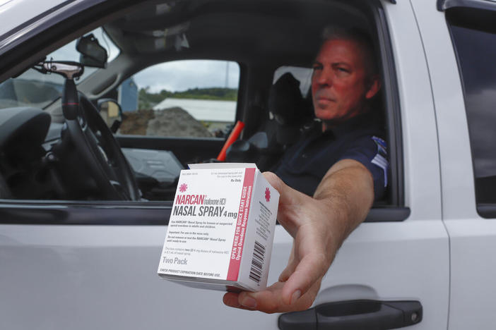 A police officer holds a box of Narcan out the driver side window of his police car.