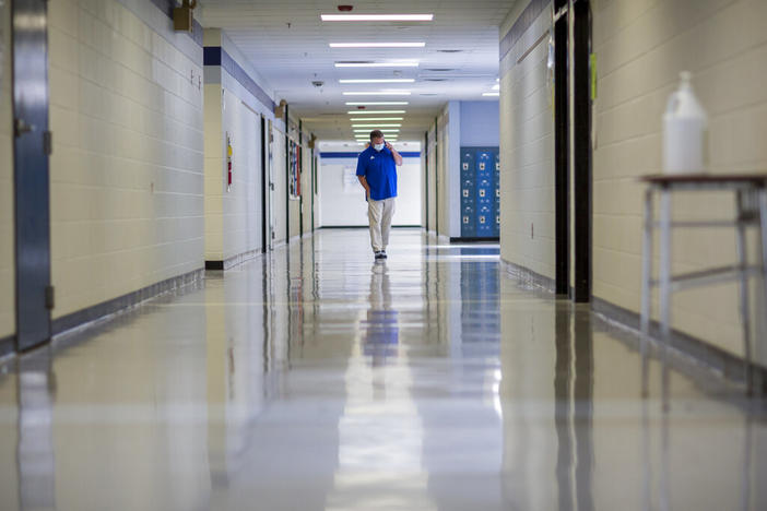 A middle school principal walks the empty halls of his school as he speaks with one of his teachers to get an update on her COVID-19 symptoms, Friday, Aug., 20, 2021, in Wrightsville, Ga. On Monday, Dec. 27, 2021, U.S. health officials cut isolation restrictions for Americans who catch the coronavirus from 10 to five days, and also shortened the time that close contacts need to quarantine.