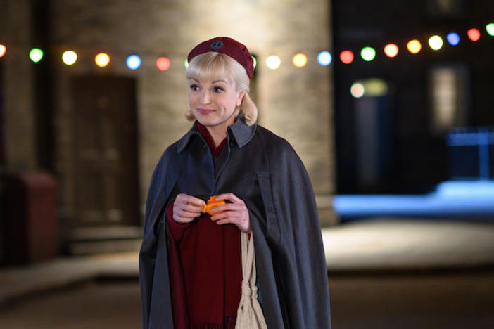 Nurse Trixie in uniform on a street lit with Christmas lights.