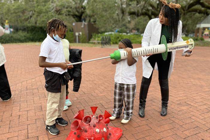 Cali Bell pretends to give her brother Calvin Bell a giant COVID-19 shot at a vaccine clinic in New Orleans, with some help from Louisiana Region One medical director Shantel Hébert-Magee.