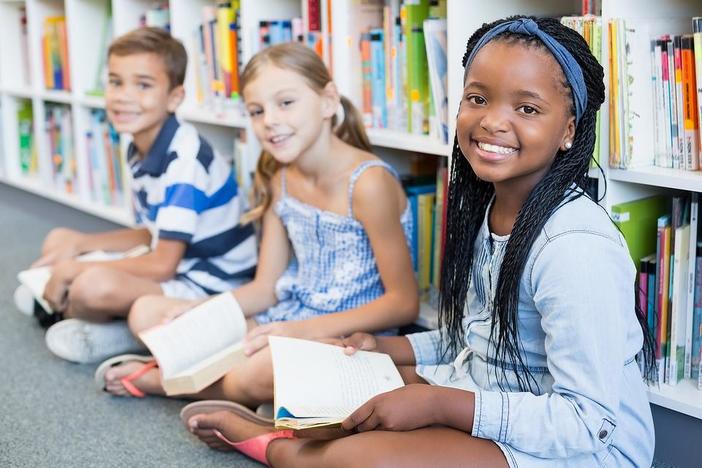 Children seated inside of a library, holding books and smiling.