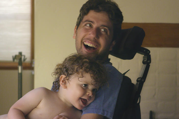 A man in a wheelchair holds his young son.