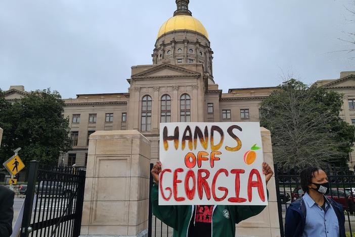 A protester holds a "hands off Georgia" sign protesting legislation that would restrict schools from teaching about racism.