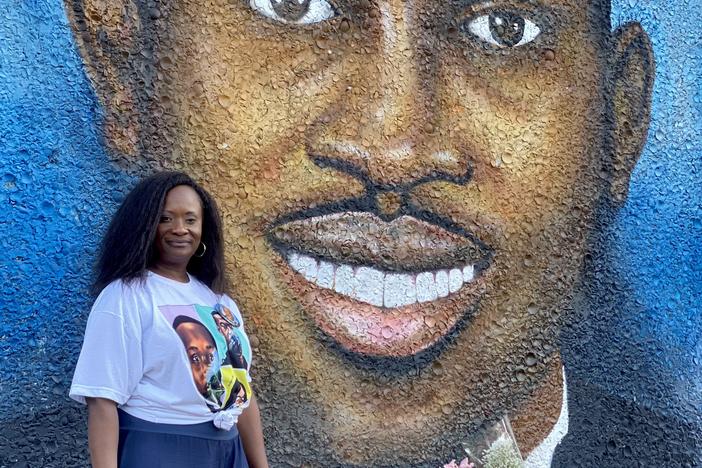 Brunswick resident Dana Roberts Beckham poses next to a mural of Ahmaud Arbery on the side of a building in Brunswick. In the mural, Arbery is wearing a black tuxedo and a white collared shirt.