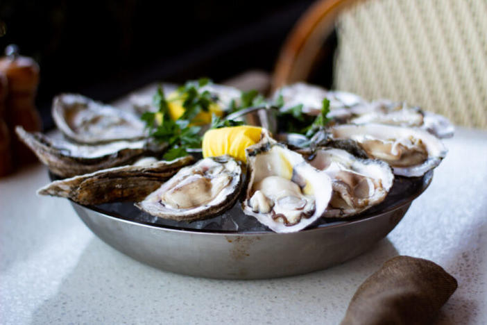 A plate of fresh, raw oysters with lemon and parsley sits on a table at C&S Seafood & Oyster Bar.