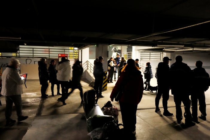 People stand in an underground parking used as a bomb shelter in a mall center in Odesa, Ukraine, Monday, Feb. 28, 2022. In makeshift shelters and underground railway platforms across Ukraine, families trying to protect the young and old and make conditions bearable amid the bullets, missiles and shells outside.