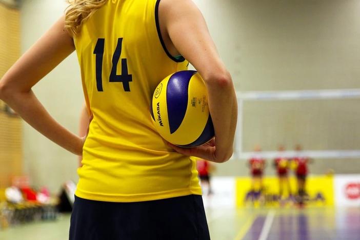 A female volleyball player stands on court.