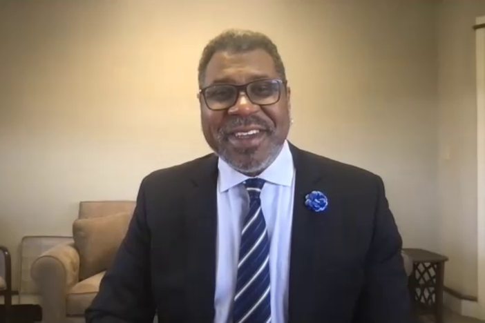 A screenshot from a Zoom interview with Gene Dobbs Bradford, the new executive director of the Savannah Music Festival. He is sitting in his office, wearing a black suit and smiling at the camera.