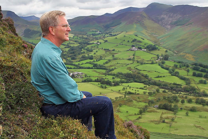 Rick Steves sitting on a mountainside.