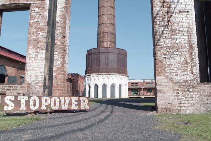 A large wooden sign reads “Stopover” in bold capital letters. It is situated on the ground, outside the Georgia State Railroad Museum in Savannah.