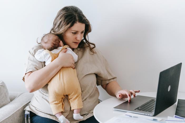 Woman works on laptop while holding an infant.