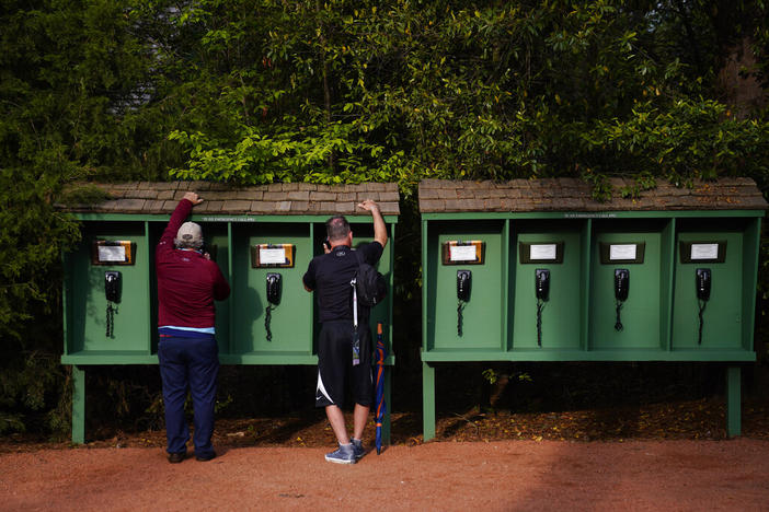 With mobile phone prohibited on the Augusta National Golf Course, spectators use phones provided by the club near the seventh hole during a practice round for the Masters golf tournament on Tuesday, April 5, 2022, in Augusta, Ga.