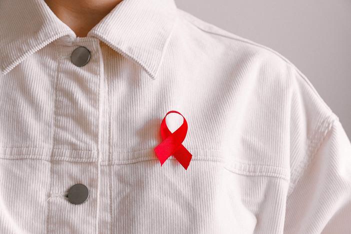 A close-up of a person in a white buttoned shirt with a red AIDS ribbon.