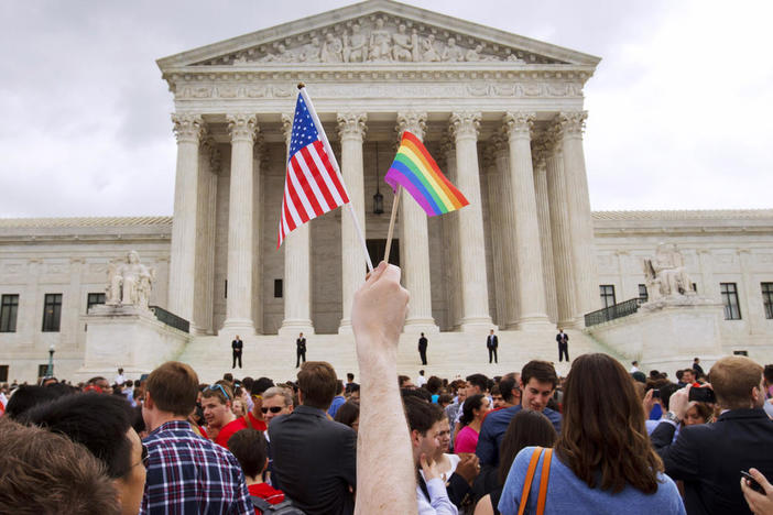 In this June 26, 2015 file photo, a man holds a U.S. and a rainbow flag outside the Supreme Court in Washington after the court legalized gay marriage nationwide. Court documents show the state of Alaska for years maintains a discriminatory policy that denied some same-sex spouses benefits by wrongly claiming gay marriage was not recognized in Alaska, long after courts ordered they be recognized.