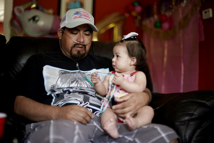 A man holds his 8-month-old daughter while on oxygen