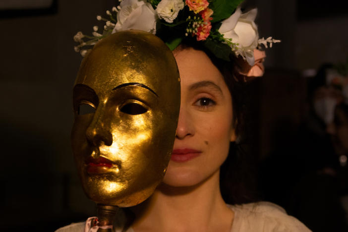 A woman's face is half obscured by a golden mask.