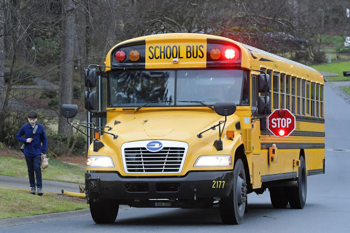 Cobb County School bus moves on street Friday, March 13, 2020, in Kennesaw, Ga. Georgia's second-largest school district on Thursday, July 14, 2022 approved a policy allowing some employees who aren't certified police officers carry guns in schools, but excluded teachers from those who can be armed. (AP Photo/Mike Stewart, File)