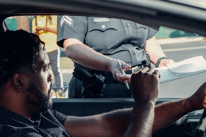 A man in his vehicle receives a traffic ticket from a police officer.