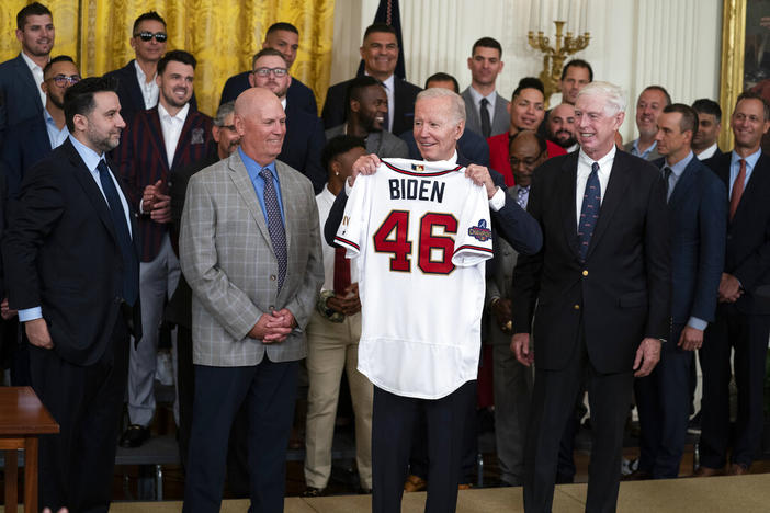 President Joe Biden holds up a jersey during an event celebrating the 2021 World Series champion Atlanta Braves, in the East Room of the White House, Monday, Sept. 26, 2022, in Washington. From left, Braves President of Baseball Operations Alex Anthopoulos, manager Brian Snitker, Biden, and Braves President and CEO Terry McGuirk. 