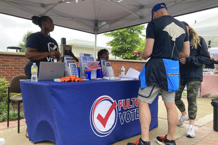 People visit a booth set up by Fulton County to recruit new poll workers at the Alpharetta Farmers Market on Sept. 10, 2022, in Alpharetta, Ga. Lies about the integrity of the 2020 presidential contest by former President Donald Trump and his allies are spurring new interest in working the polls in Georgia and elsewhere in the nation for the upcoming midterm elections.