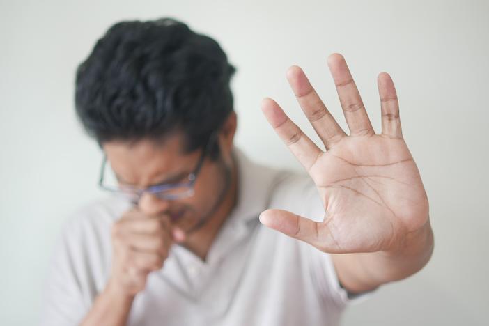 A coughing man puts his hand out to keep people away