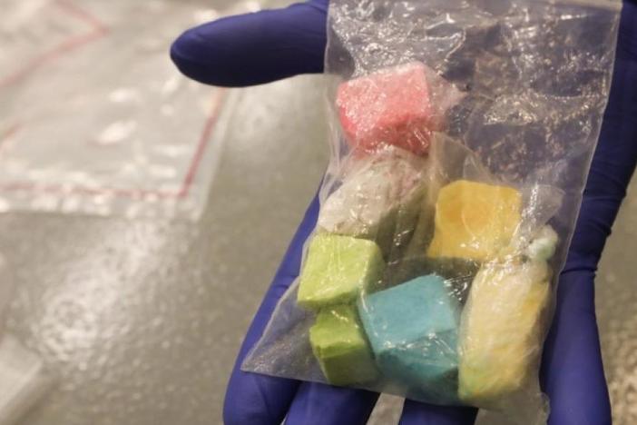 A gloved hand holding a bag of colored fentanyl candy.