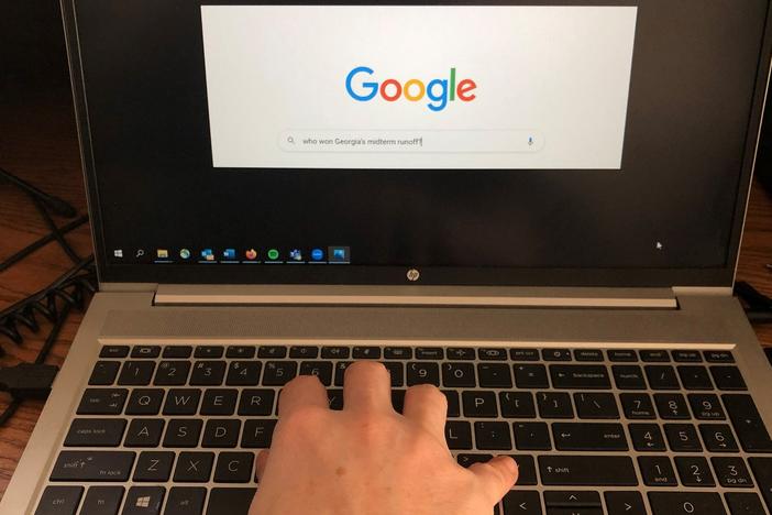 A hand types a search query on Google