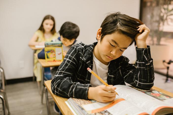 Boy at a school desk reading with a hand on his head and a pencil in his right hand