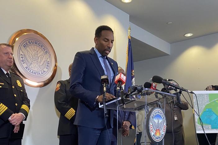 Atlanta Mayor Andre Dickens is shown standing behind a podium and speaking into microphones, flanked by police officials.