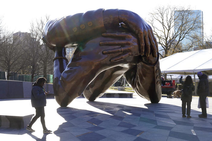 Passers-by walk near the 20-foot-high bronze sculpture "The Embrace," a memorial to Dr. Martin Luther King Jr. and Coretta Scott King, in the Boston Common, Tuesday, Jan. 10, 2023, in Boston. The sculpture, consisting of four intertwined arms, was inspired by a photo of the Kings embracing when MLK learned he had won the Nobel Peace Prize in 1964. The statue is to be unveiled during ceremonies Friday, Jan. 13, 2023.