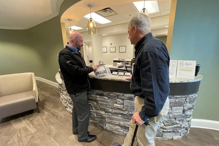 Dr. Daniel Cobb and Chris Griffin, his patient, speak at the counter in the lobby of the Neuro Center in Gainesville, Georgia.