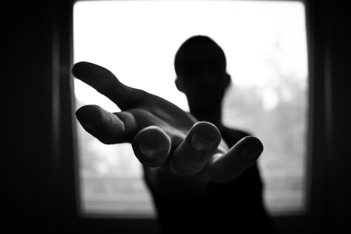 A backlit photo of a person extending a hand