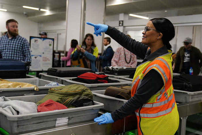 A worker points as people wait for the belongings at the Transportation Security Administration security area at the Hartsfield-Jackson Atlanta International Airport on Wednesday, Jan. 25, 2023, in Atlanta.