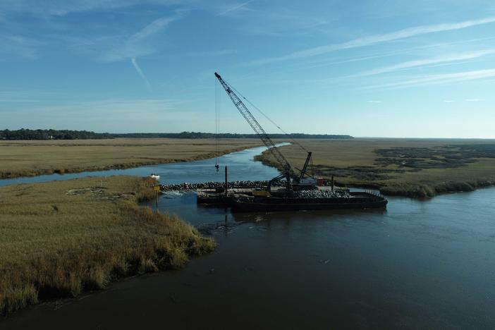 Two rivers are shown in an aerial view with heavy construction equipment floating on the water.