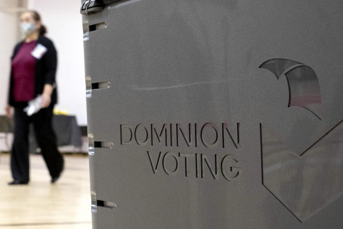 A worker passes a Dominion Voting ballot scanner while setting up a polling location at an elementary school in Gwinnett County, Ga., outside of Atlanta on Jan. 4, 2021. Newsmax has apologized to an employee of Dominion Voting Systems for airing false allegations that he manipulating voting machines or tallies on Election Day to the detriment of former President Donald Trump. Eric Coomer, security director for Dominion, subsequently dropped the conservative news network from a defamation lawsuit. (AP Photo/