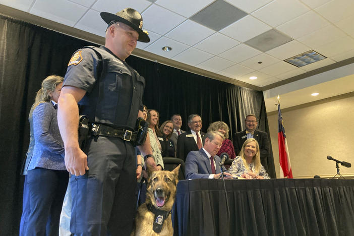 Georgia State Trooper Trent Kirchhefer stands with K-9 officer Vilma as Gov. Brian Kemp signs a bill clarifying penalties for harming a police dog, Wednesday, April 26, 2023, at Lake Lanier Islands in Buford, Ga. Kemp signed a number of public safety bills including one stiffening penalties for gang crimes and recruiting gang members. 