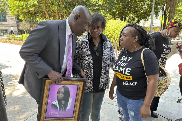 An attorney holding a picture of a young woman is shown talking with two women.