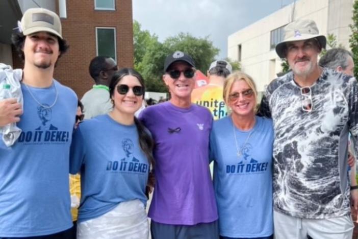 Five people are shown posing for a photo in T-shirts during a walk for cancer research.