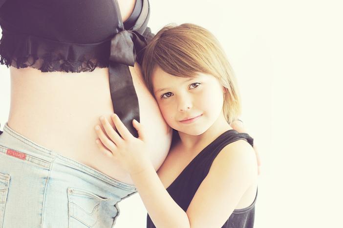 A young girl presses her ear to a woman's pregnant belly