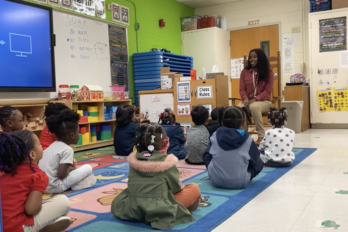 Children listening to teacher intently while sitting together on the floor.