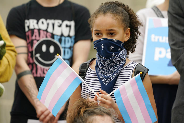 A young child holds a pair of trans pride flags at a noon gathering on the steps of the Mississippi Capitol in Jackson, as they protest House Bill 1125, which bans gender-affirming care for trans children, Wednesday, Feb. 15, 2023.